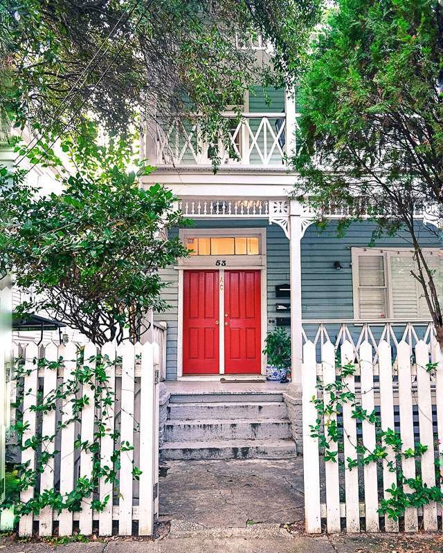 Bright blue home with white trim, bright red door, ivy covered white picket fence
